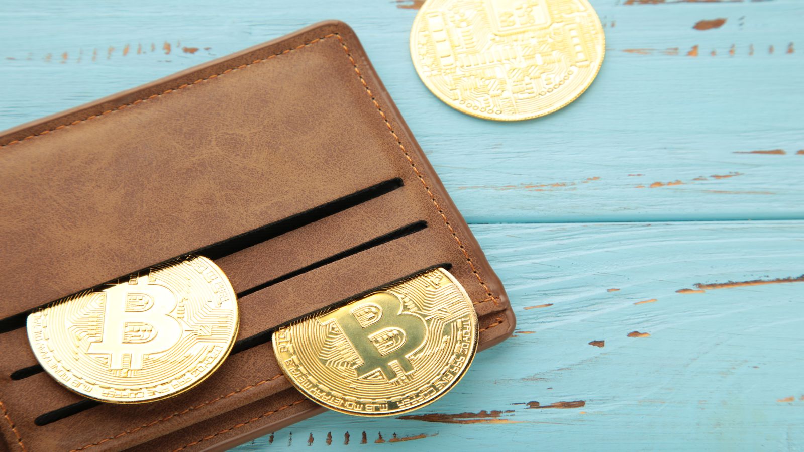 A balanced scale on a dark desk surface with a gold coin on one side and a small engraved Bitcoin token on the other, soft directional lighting