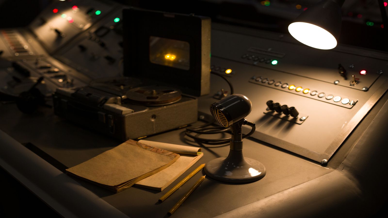 A clean studio desk with a microphone, headphones, and a warm desk lamp, representing the Flirting With Bitcoin recording space